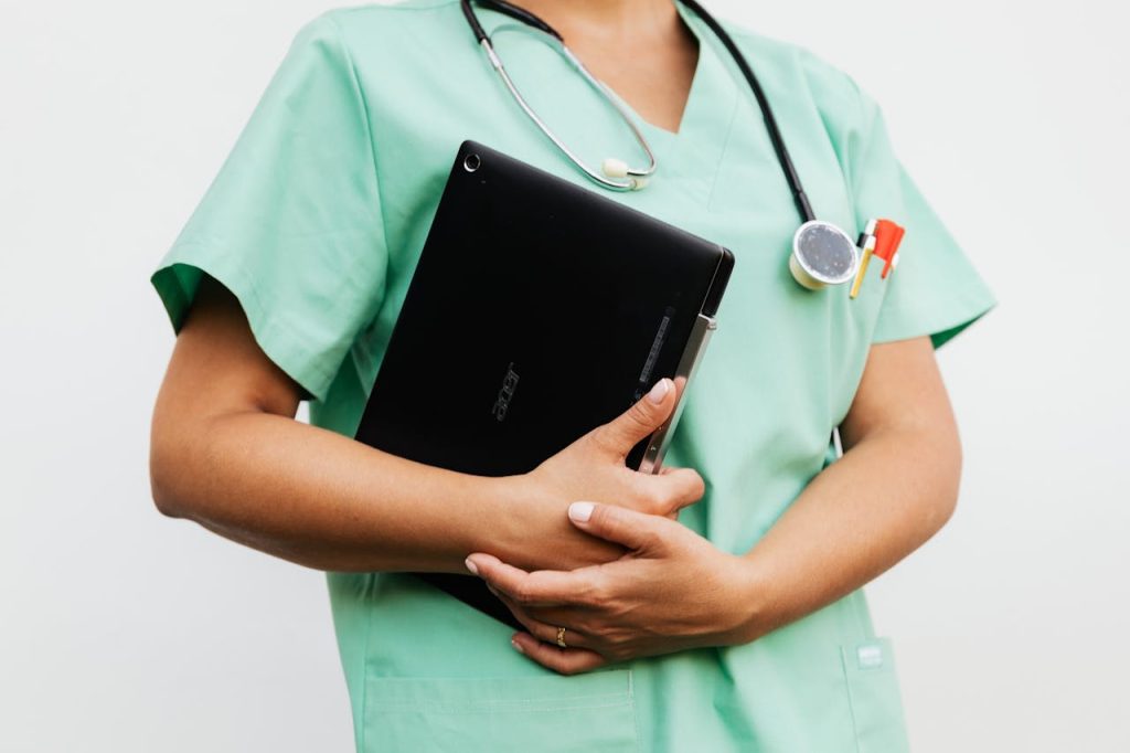 a-doctor-holding-a-digital-tablet-5206922 Close-up of a nurse in green scrubs holding a tablet and stethoscope, symbolizing modern healthcare.