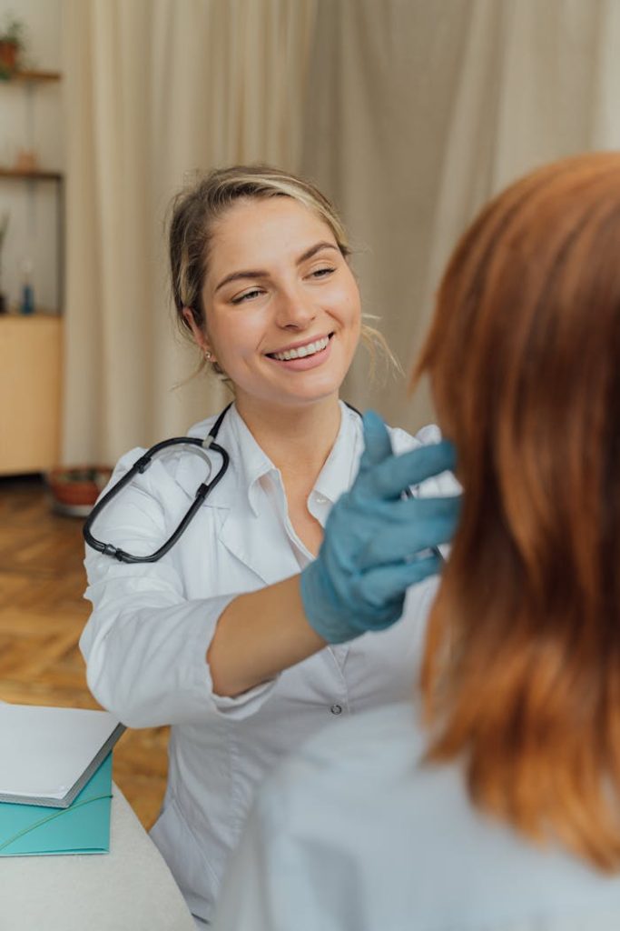 a-woman-in-white-long-sleeve-shirt-smiling-5215017 A cheerful healthcare professional examining a patient indoors, promoting positive healthcare experiences.