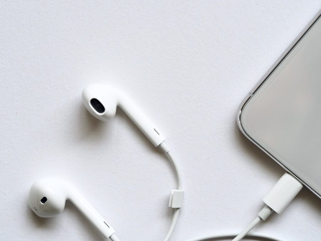 apple-earpods-983831 Minimalist top view of white wired earphones connected to a smartphone on a clean white background.