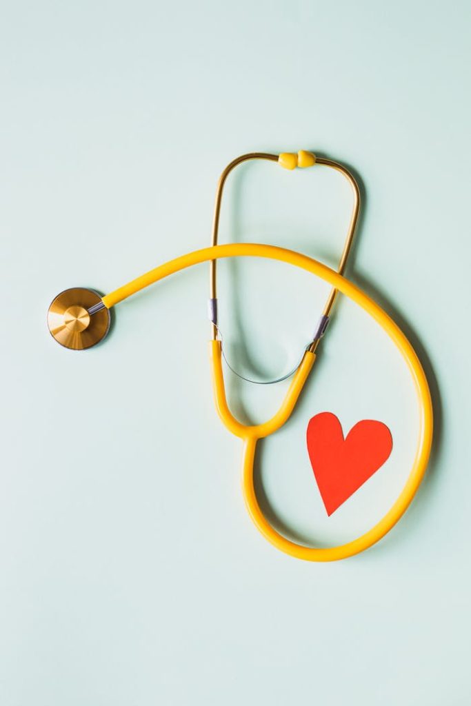 medical-stethoscope-with-red-paper-heart-on-white-surface-4386467 Yellow stethoscope arranged with a red heart cutout on a light green background, symbolizing heart health.